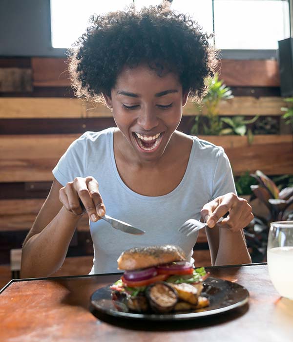 Beautiful african american woman eating a delicious bagel with vegetables at a restaurant looking happy and very hungry